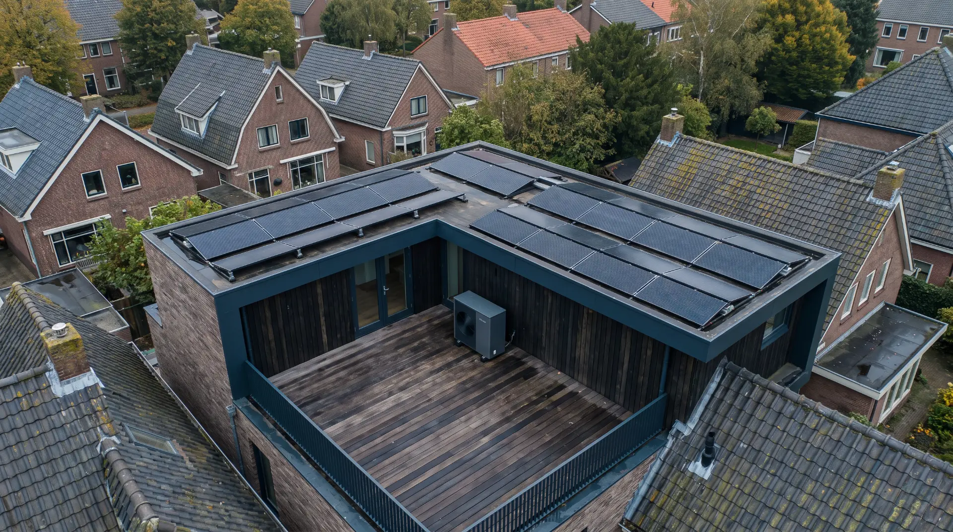 Warmtepomp buitenunit op een plat dak naast zonnepanelen bij een woning
