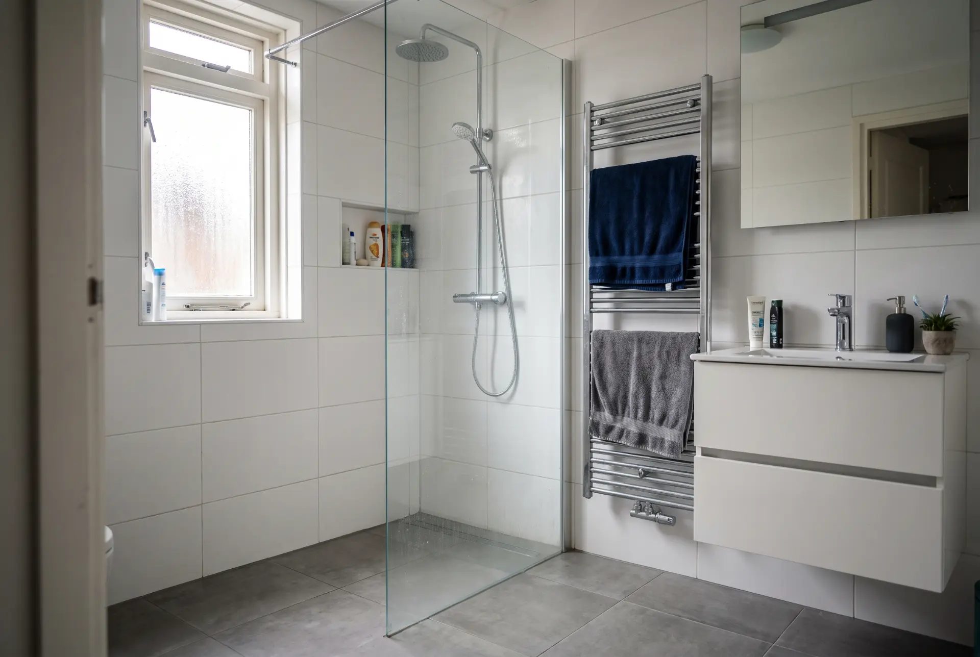 Lichte badkamer met glazen inloopdouche, handdoekradiator en wastafelmeubel